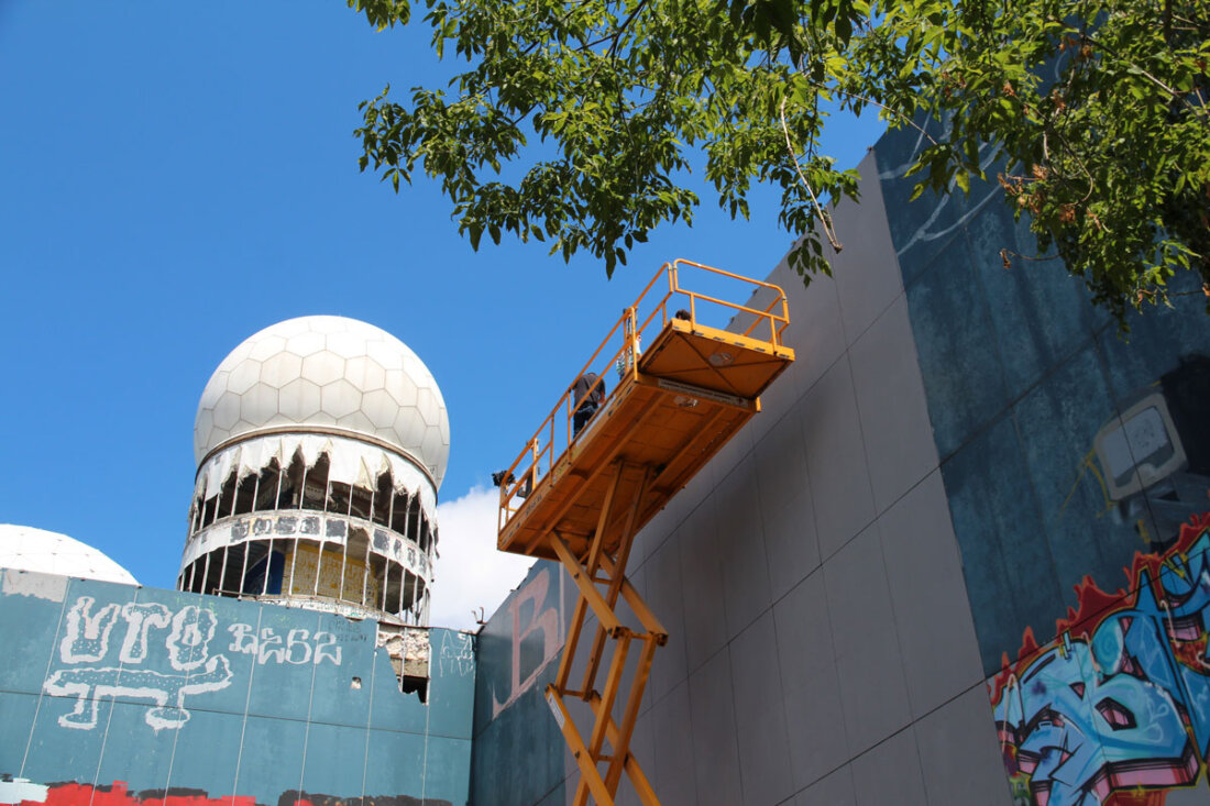 Artist painting a facade mural from an aerial lift