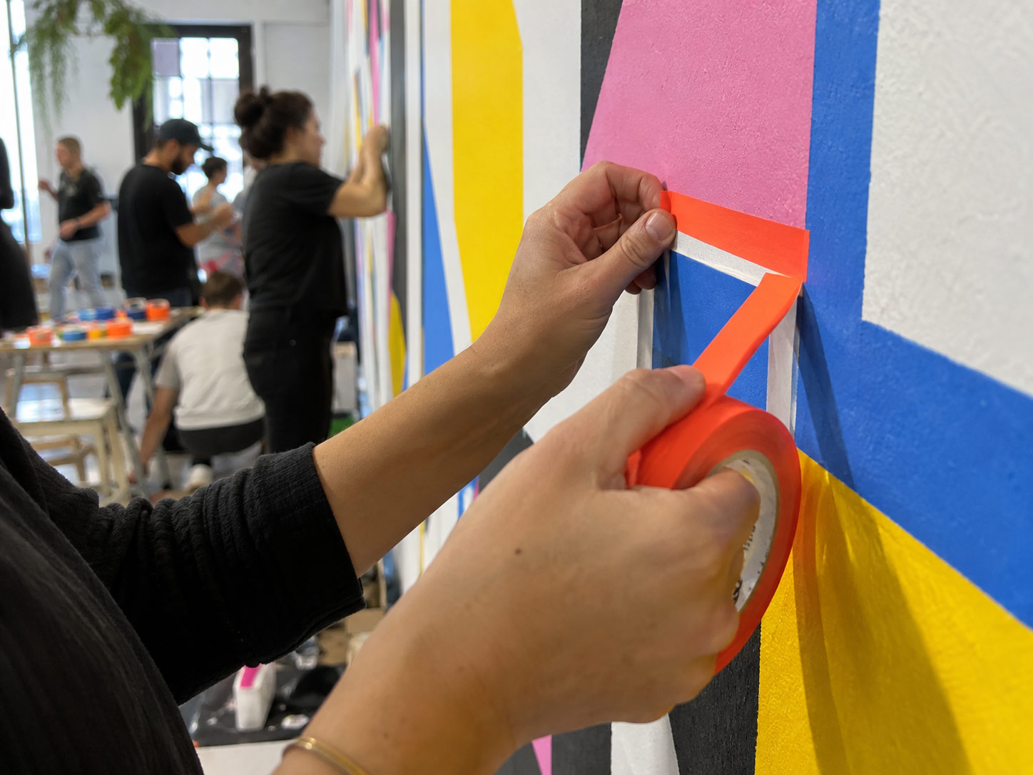 Close-up: hands pulling orange tape into a line on the wall