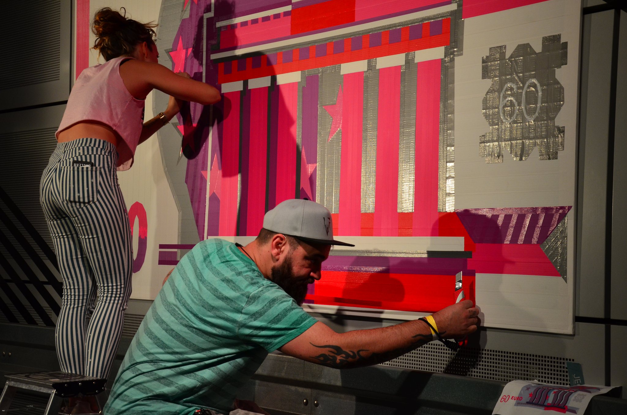 Two crew artists taping a large tape art motif on a wall
